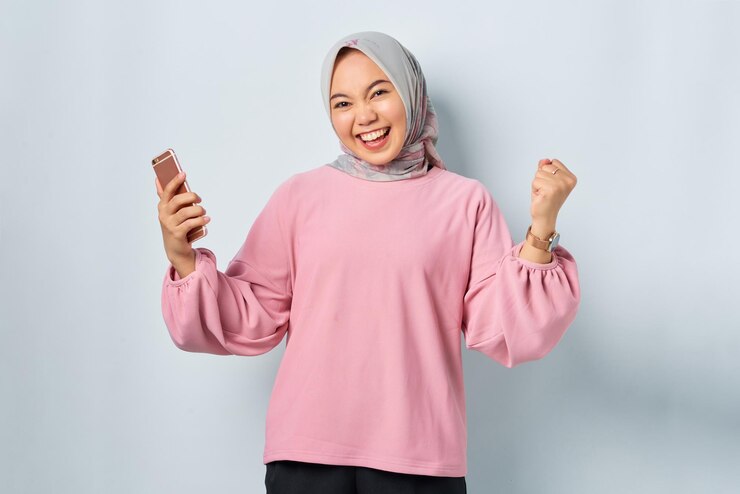 Excited young Asian woman in pink shirt using mobile phone received good news isolated over white background
