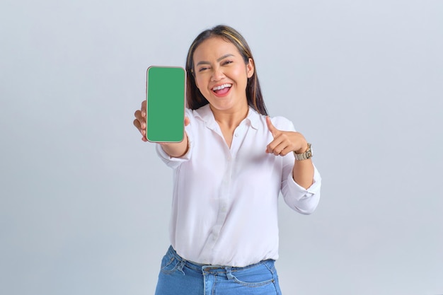흰색 배경에 격리된 모바일 앱을 추천하는 빈 화면 휴대폰을 보여주는 흥분된 젊은 아시아 여성