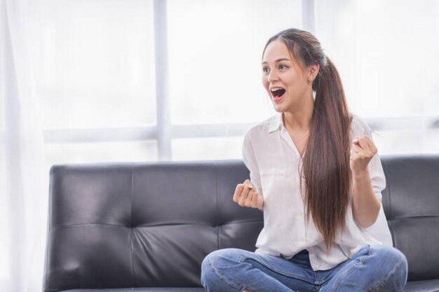 自宅のオフィスのソファで興奮した若いアジア人女性