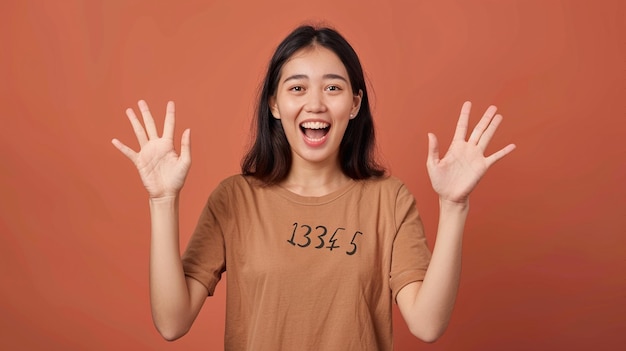 Foto giovane donna asiatica eccitata con le mani in alto su uno sfondo marrone