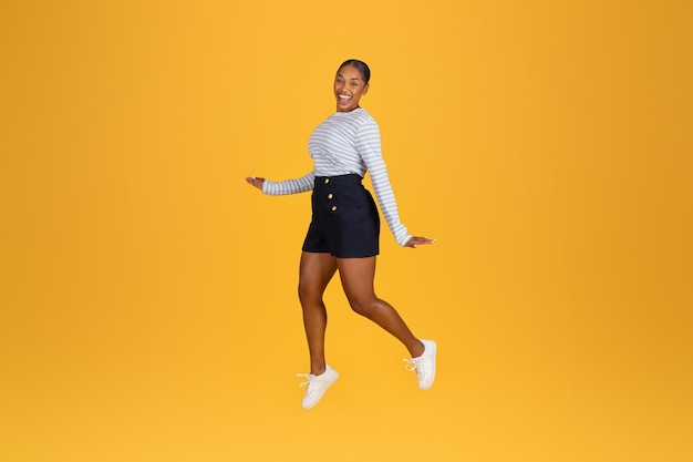 Excited young black woman jumping in the air on yellow