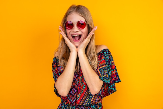 Excited young blonde slavic girl with sunglasses putting hands on her face and looking at side