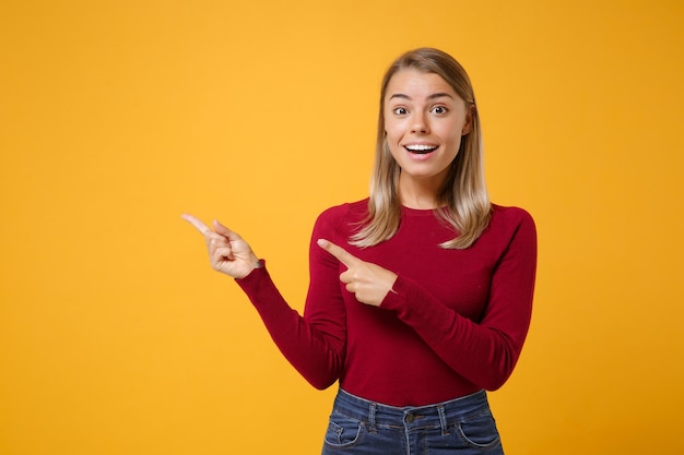 Excited young blonde woman girl in casual clothes posing isolated on yellow orange background studio portrait. People emotions lifestyle concept. Mock up copy space. Pointing index fingers aside up.