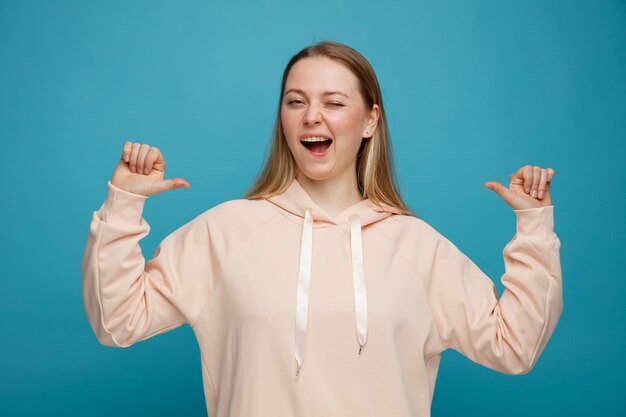 Excited young blonde woman winking pointing at herself 