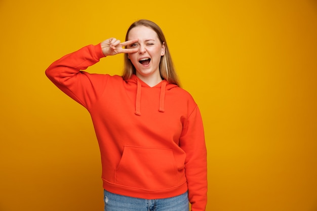 Photo excited young blonde woman winking showing v-sign symbol near eye