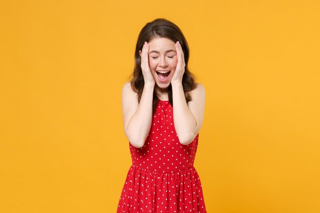 Excited young brunette woman girl in red summer dress posing isolated on yellow background studio pe