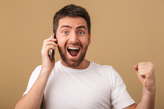 Excited young casual man talking on mobile phone isolated