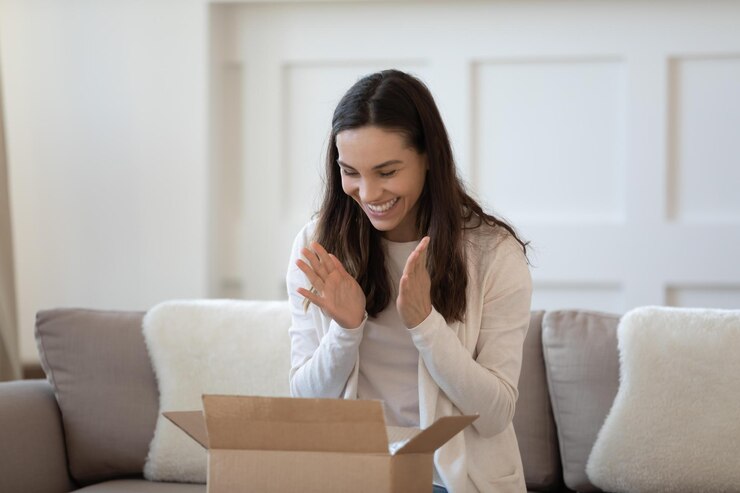 Photo excited young caucasian woman sit on sofa at home feel euphoric unbox internet order package happy millennial female unpack box shopping online satisfied with good quality product delivery concept