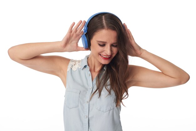 Excited young Caucasian woman in sleeveless shirt listening to music in blue wireless headphones