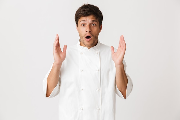 Excited young chef man standing isolated on white wall.