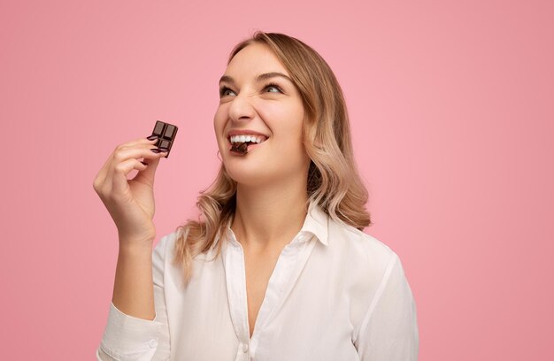 ピンクのスタジオで美味しいチョコレートをむ興奮した若い女性