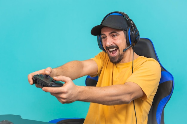 Excited young gamer man playing games holding joystick isolated on blue wall background studio