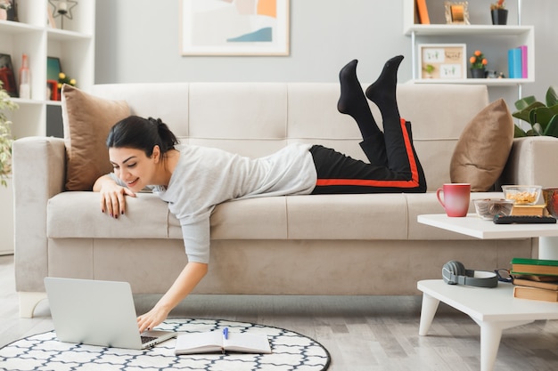 Excited young girl lying on sofa used laptop in living room