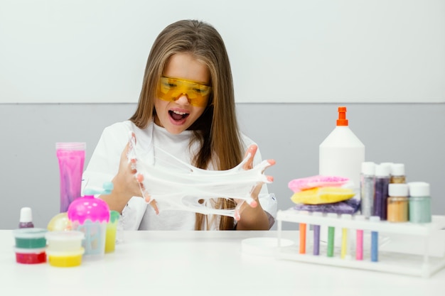 Excited young girl scientist experimenting with slime