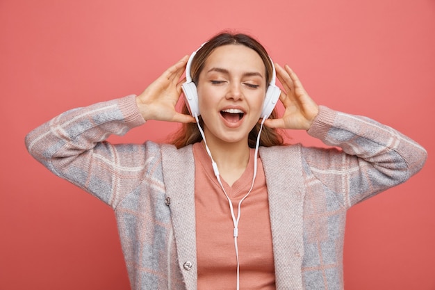 Excited young girl wearing and grabbing headphones listening to music with closed eyes 