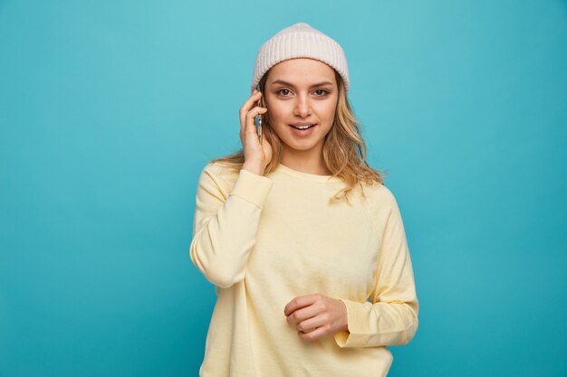 Excited young girl wearing winter hat talking on phone 