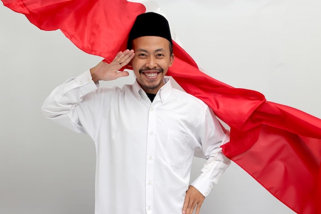 Excited young indonesian man is making a salute gesture with indonesia flag in the background