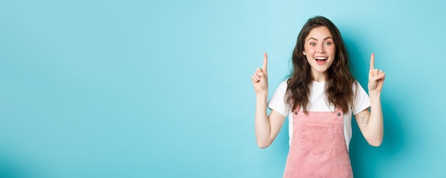 Photo excited young lively girl showing promo laughing and smiling happy pointing fingers up at top advert