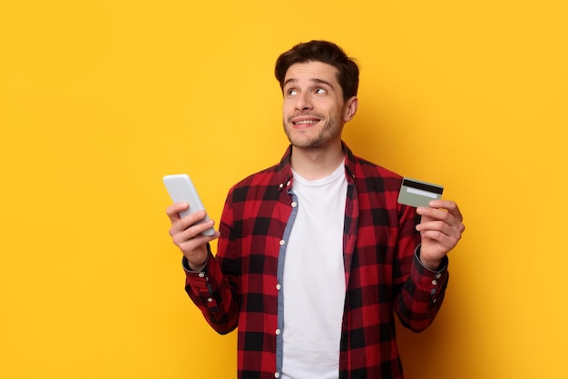 Возбужденный молодой человек с кредитной картой и мобильным телефоном