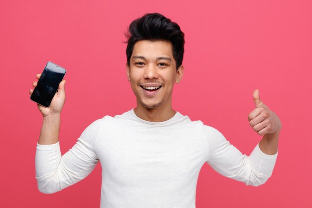 Excited young man holding mobile phone showing thumb up 