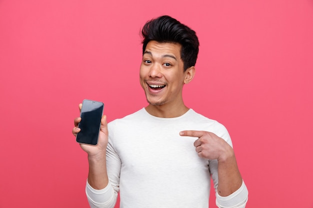 Excited young man holding and pointing at mobile phone 