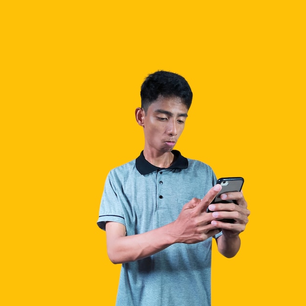 excited young man holding a smart phone wearing a gray tshirt yellow background