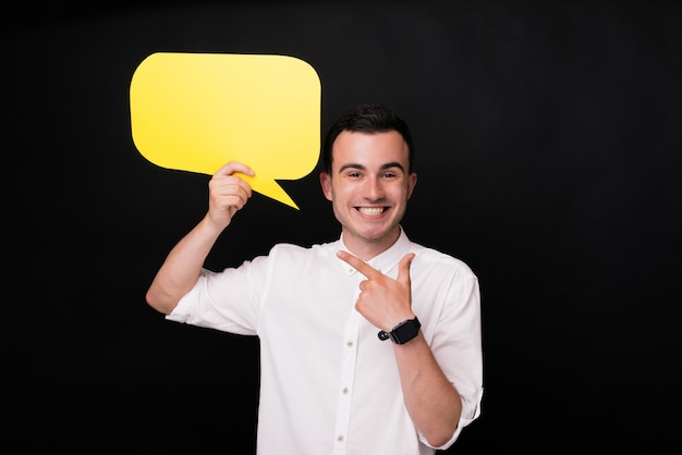 Excited young man pointing at a yellow bubble speech. Say something or leave comment.