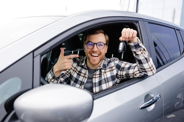 Excited young man showing a car key sitting inside his new vehicle