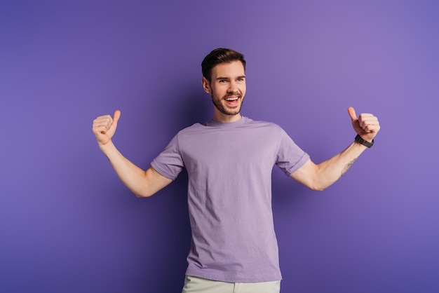 Excited young man showing thumbs up while looking away on purple background