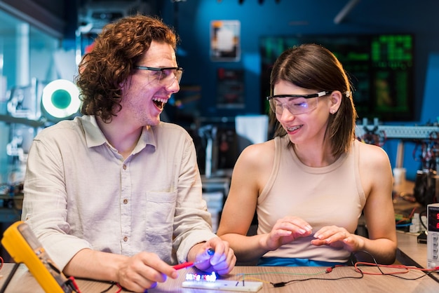 Foto eccitato giovane uomo e donna in occhiali protettivi che fanno esperimenti con l'elettricità in un laboratorio