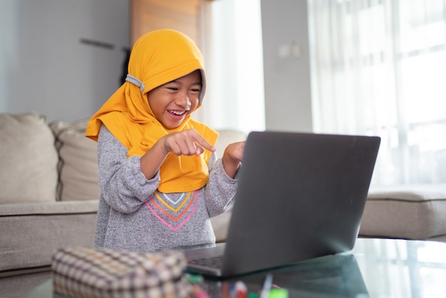 노트북을 사용하여 집에서 온라인으로 공부하는 동안 흥분된 젊은 무슬림 아이