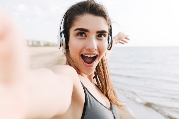 Excited young sportswoman with headphones taking a selfie