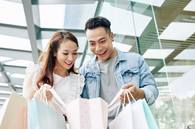 Excited young Vietnamese couple looking in paper bag after shopping in mall