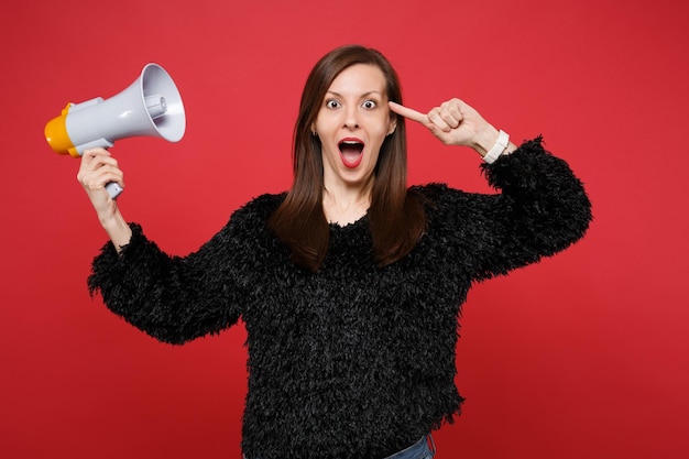 Photo excited young woman in black fur sweater pointing index finger on head, hold megaphone isolated on bright red wall background in studio. people sincere emotions, lifestyle concept. mock up copy space.