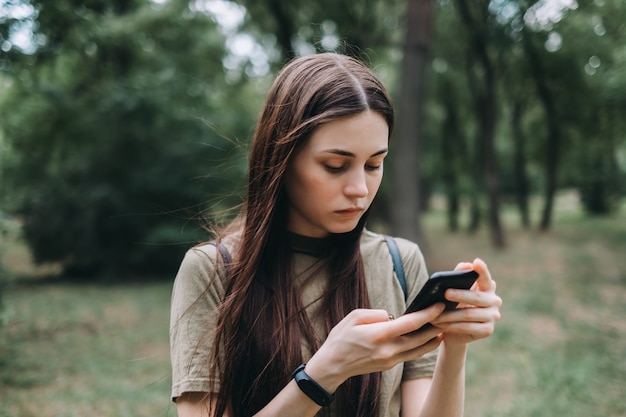 Excited young woman in the city park using smartphone and typing text.