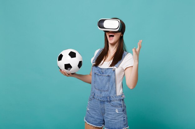 Excited young woman football fan looking in headset holding\
soccer ball playing isolated on blue turquoise wall background.\
people emotions, sport family leisure lifestyle concept. mock up\
copy space.