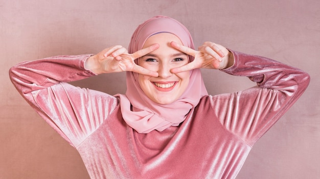 Excited young woman gesturing v sign near eyes looking at camera