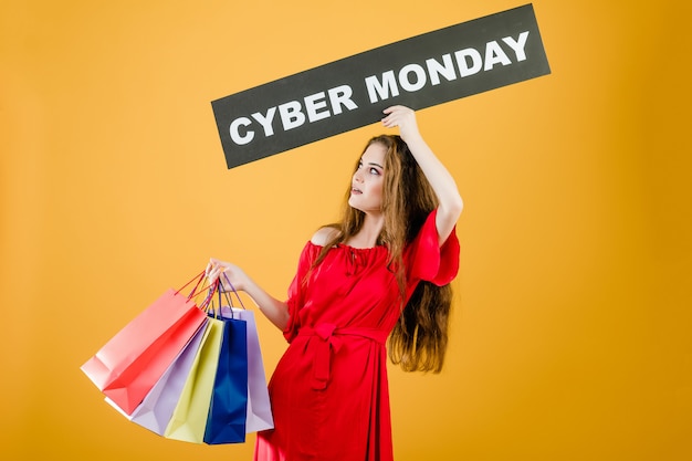 Excited young woman has cyber monday sign with colorful shopping bags isolated over yellow