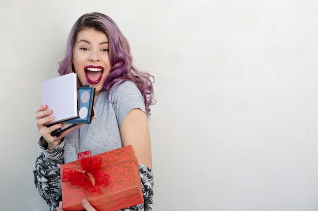 Excited young woman holding gift box with cosmetic palettes, studio shot over a grey background. Copy space