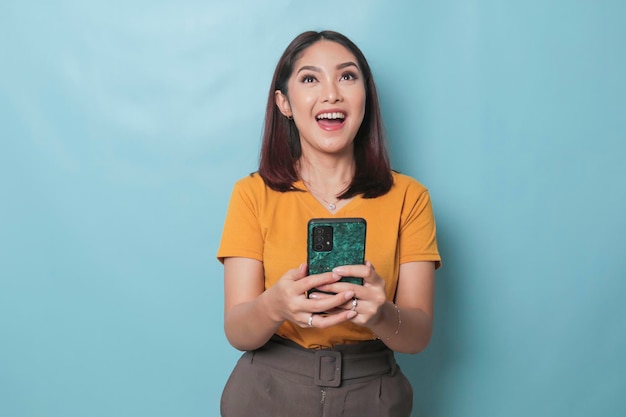 Una giovane donna eccitata sorride mentre tiene il suo smartphone in mano isolato su sfondo blu