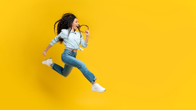 Excited young woman jumping up at orange studio