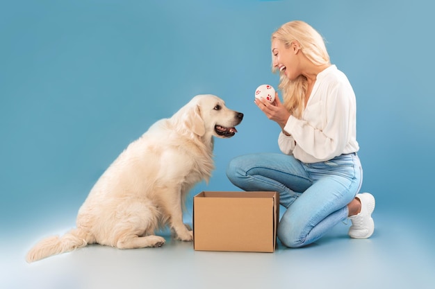 Excited young woman playing with dog holding ball