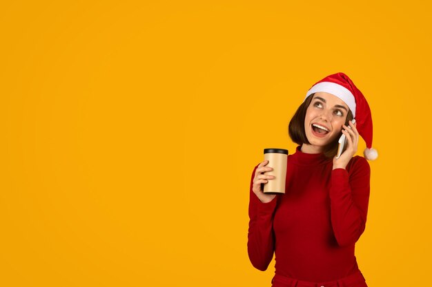 Excited young woman in Santa hat having phone conversation