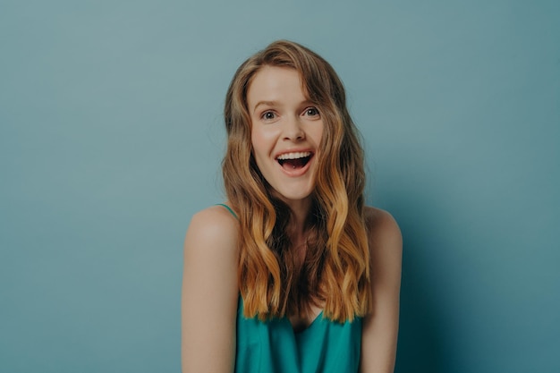 Excited young woman showing on camera positive surprised facial expression and broadly toothy smile