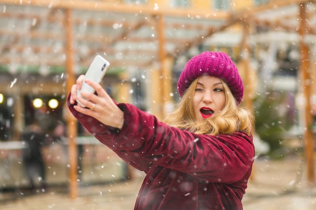 Excited young woman taking selfie at the street winter market