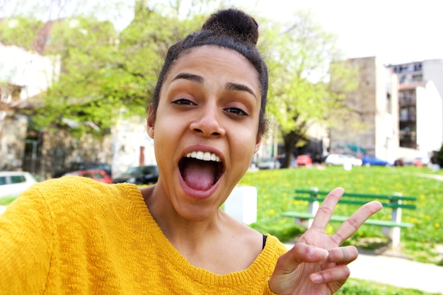 Excited young woman taking selfie with peace sign