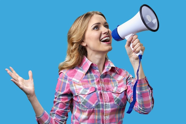 Excited young woman talking into megaphone on color background holiday sales