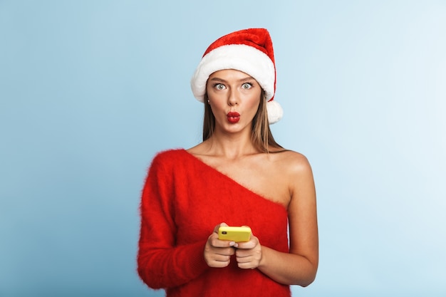 Excited young woman wearing christmas hat, using mobile phone.