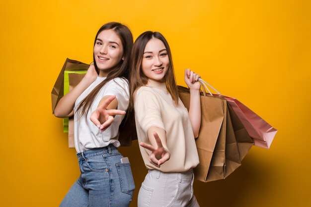 Excited young women girls friends hold package bag with purchases after shopping posing isolated on yellow wall . people lifestyle concept.