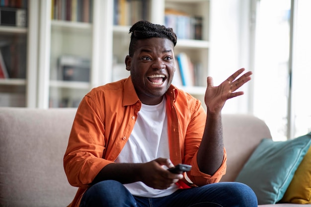 Exciting african american guy sitting at home watching tv